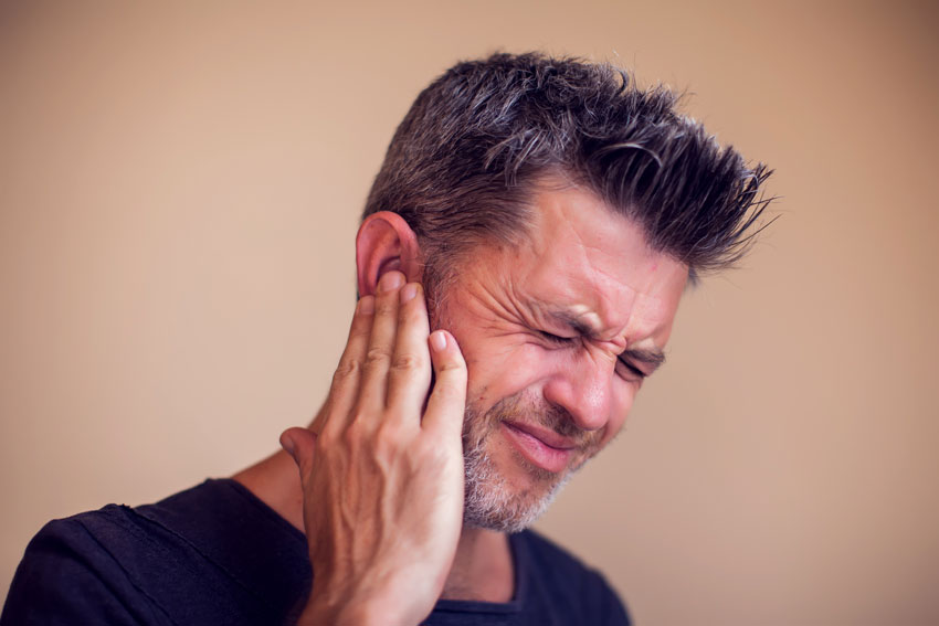adult man holding his ear in pain, symptoms of TMJ